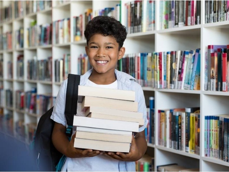 Παιδί κρατάει χαμογελώντας στοίβα βιβλίων
